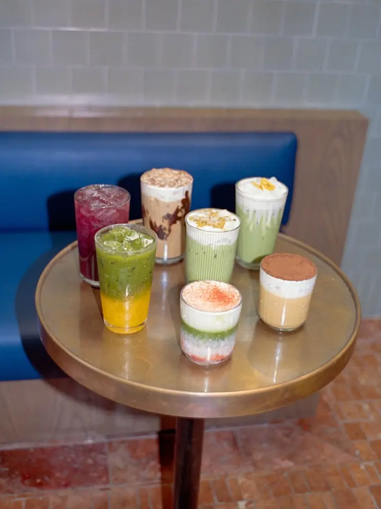 Seven iced, layered, and foamy drinks arranged on a round table