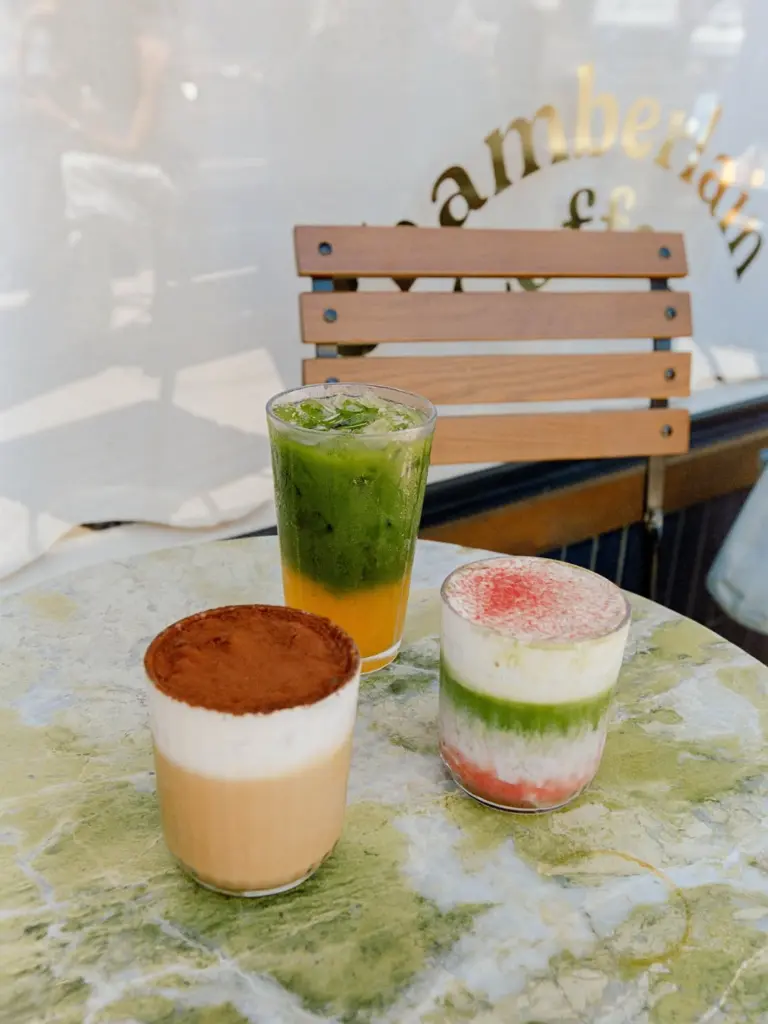 Three colorful layered drinks arranged on a marble café table