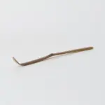 Slender brown bamboo matcha scoop with a curved tip on a white surface