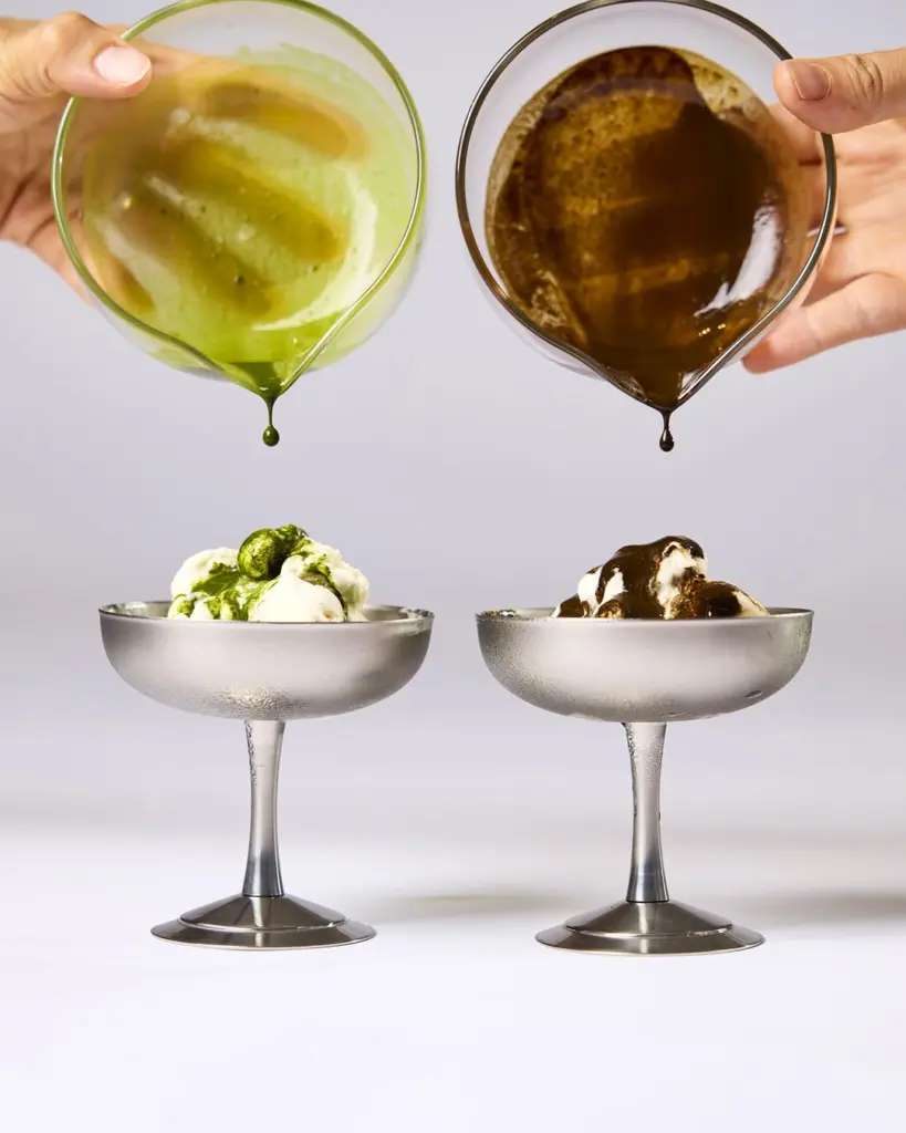 Green and brown sauces dripping from glass pitchers onto two bowls of ice cream