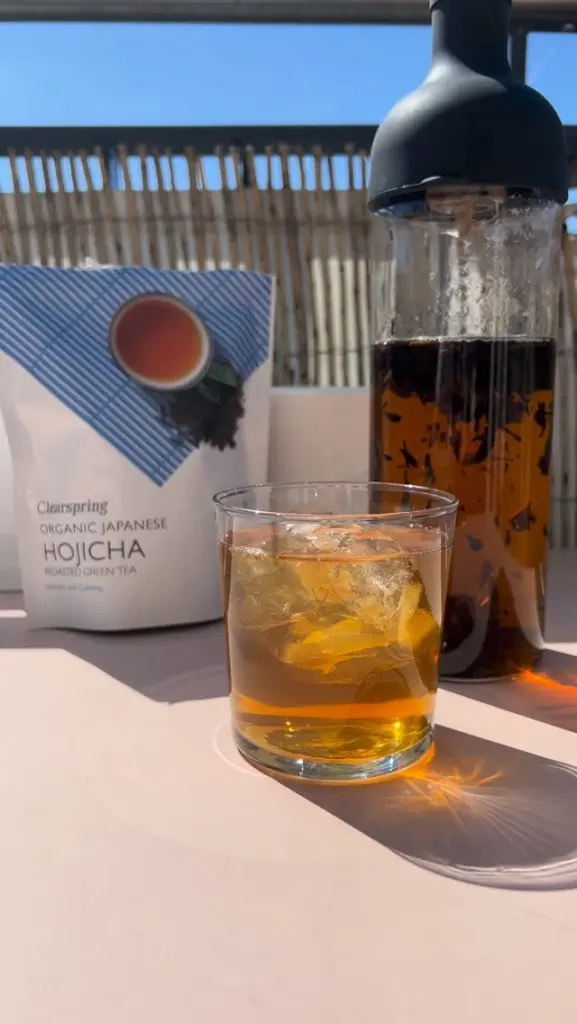 Glass of amber iced tea beside a tea infuser and Clearspring Hojicha package