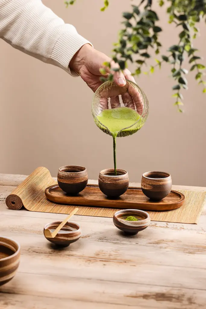 Bamboo chashaku resting across a small bowl as green matcha is poured into ceramic cups