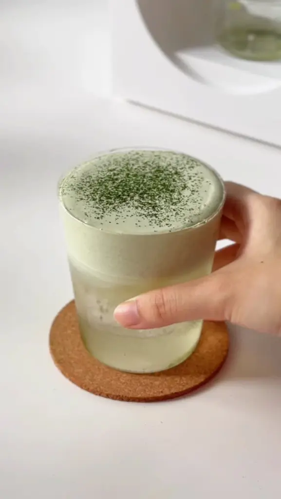 Hand holding a frothy pale green iced matcha drink