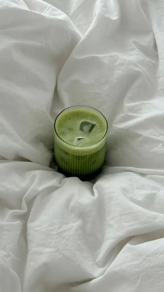 Ribbed glass of iced green matcha nestled in white bedding