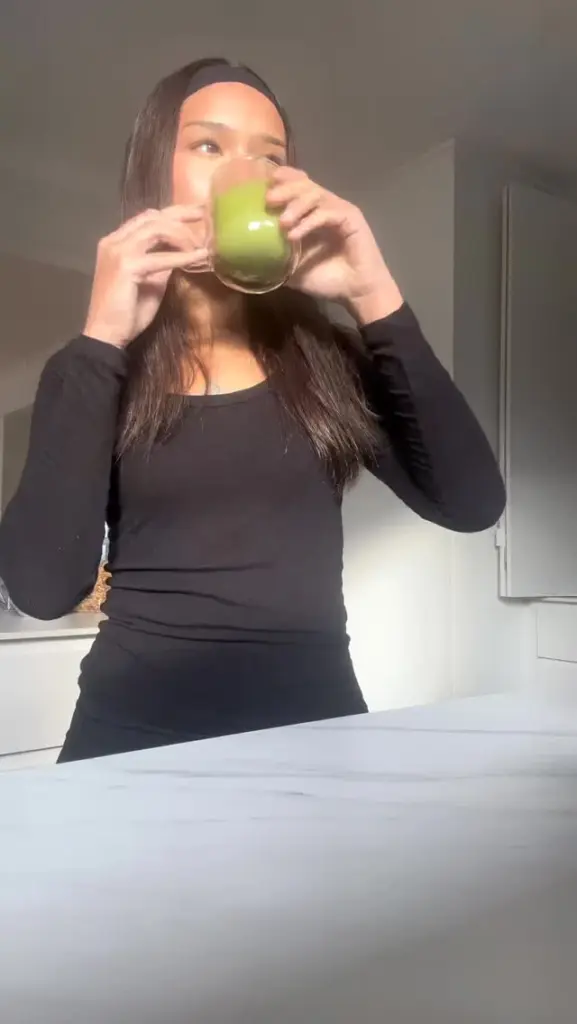 Person sipping a green drink from a clear glass mug in sunlight