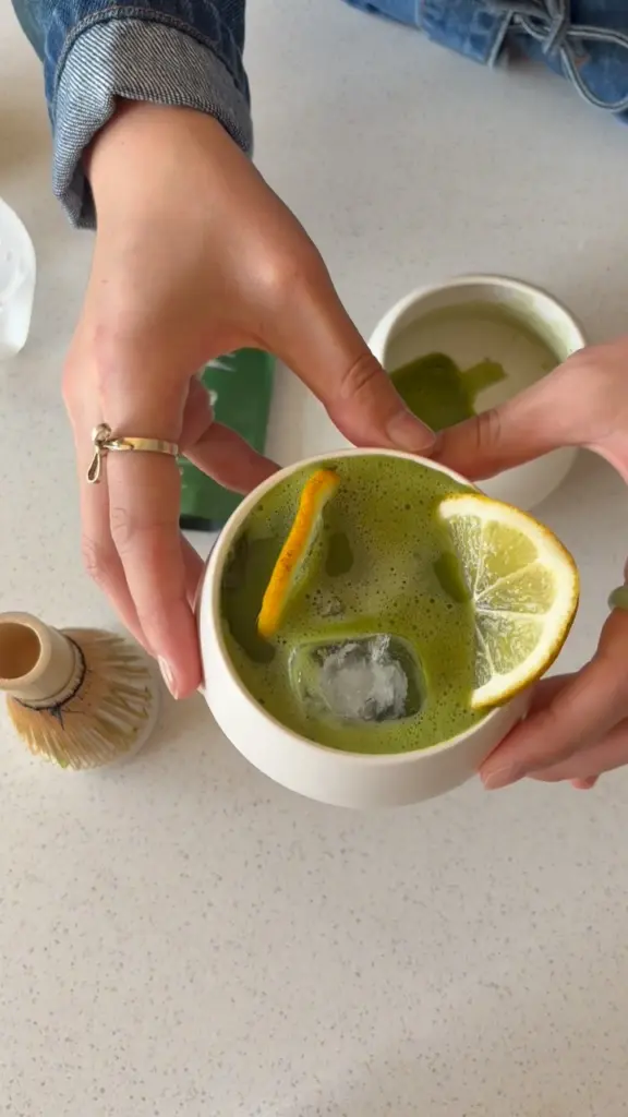 Hands holding a bowl of iced green matcha garnished with citrus slices