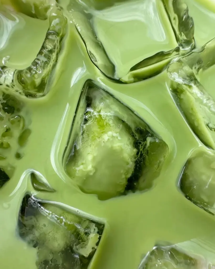 Close-up of a pale green drink flowing around clear ice cubes