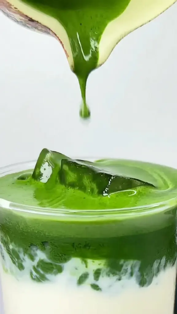 Thick green matcha pouring over ice into a layered white drink