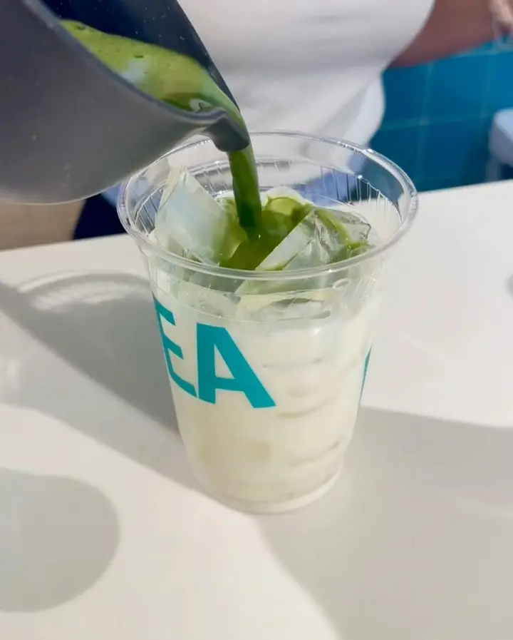 Green matcha pouring into a clear cup filled with ice and a pale drink