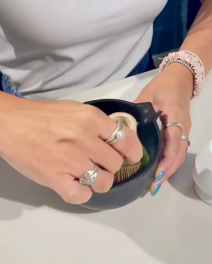 Hands whisking green matcha in a dark ceramic bowl