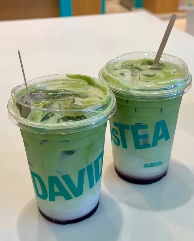 Two clear cups of layered green iced drinks on a white table