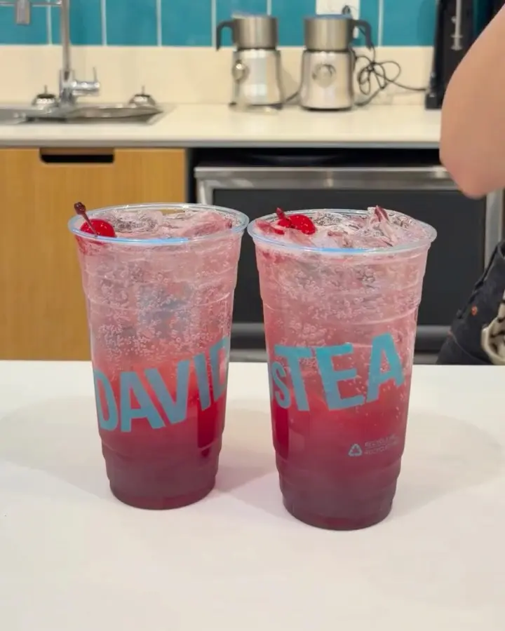 Two pink sparkling iced drinks garnished with red cherries