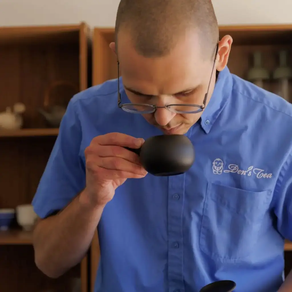 Person in a blue Den's Tea shirt smelling tea from a black cup
