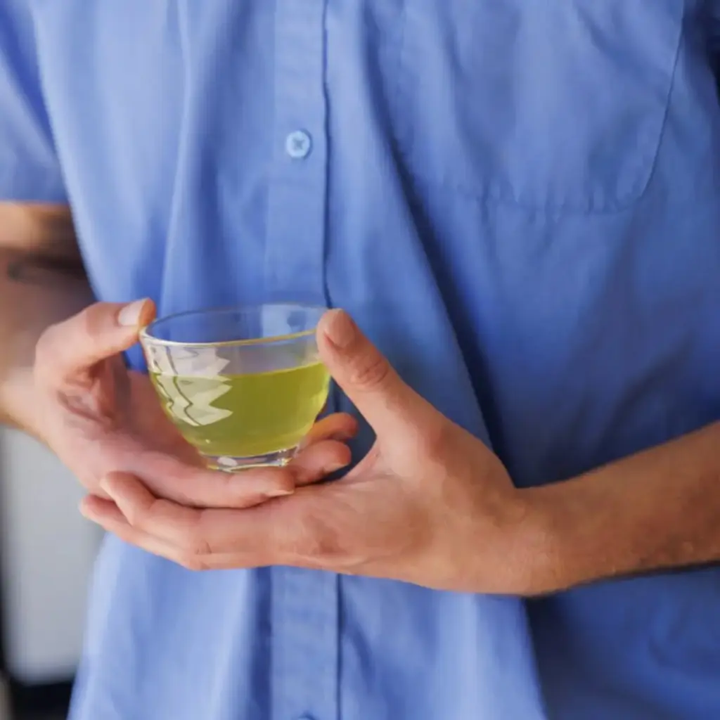 Hands cradling a clear glass cup filled with pale green tea