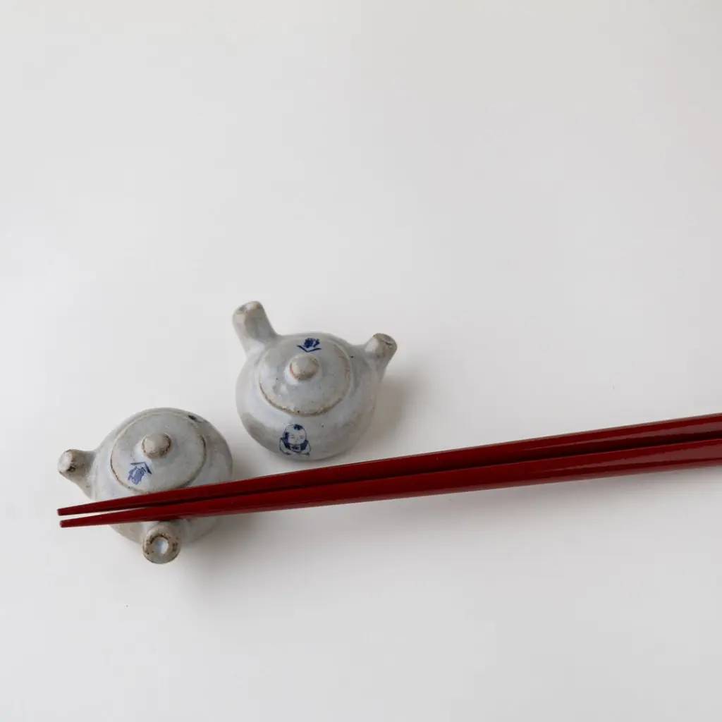 Red chopsticks laid across two small ceramic teapot-shaped rests