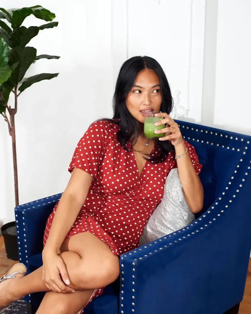 Woman in a red polka-dot dress sipping a green drink while seated in a blue armchair