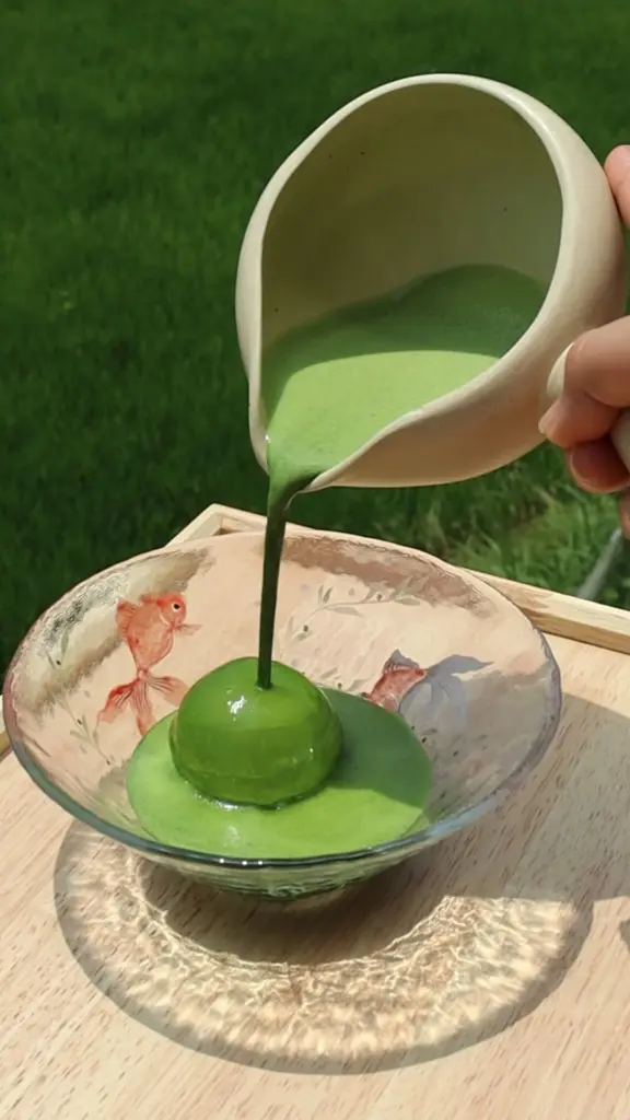 Thick green tea sauce poured over a round green dessert in a glass bowl