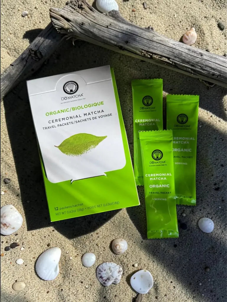 Do Matcha travel packet box and three green sachets on sand with shells and driftwood