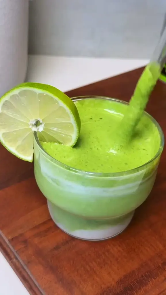Frothy bright green drink in a glass with a lime wheel on the rim