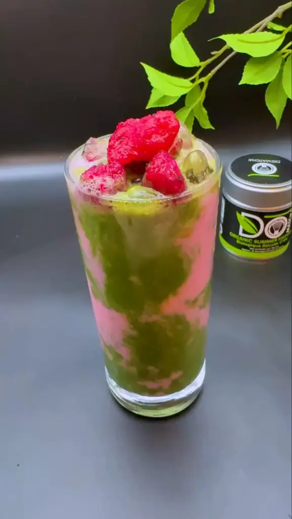 Tall iced green and pink drink topped with red berries beside a Do Matcha tin