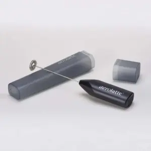 Black Aerolatte handheld whisk with a metal coil beside an open gray travel case