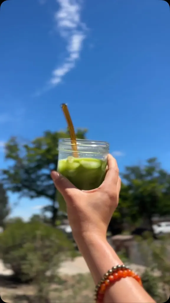 Hand holding an iced green drink with a straw against a blue sky