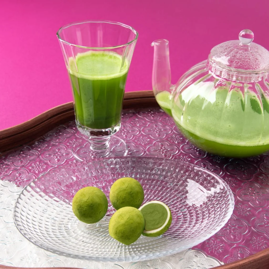 Glass teapot and cup of bright green tea beside round green confections