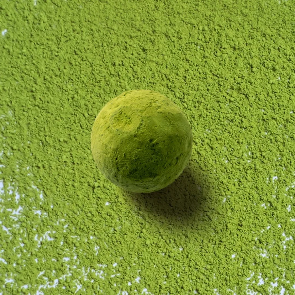 Round confection coated in green powder on a bed of matching powder