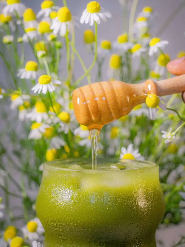 Honey dripping from a wooden dipper into an iced green drink among white flowers