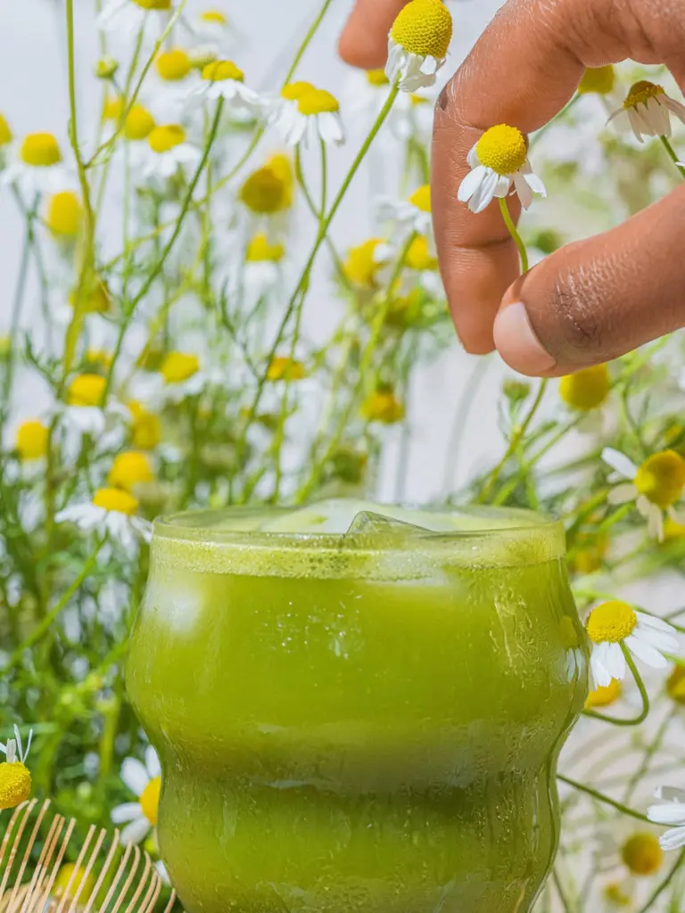 Hand holding a small white flower above an iced green drink