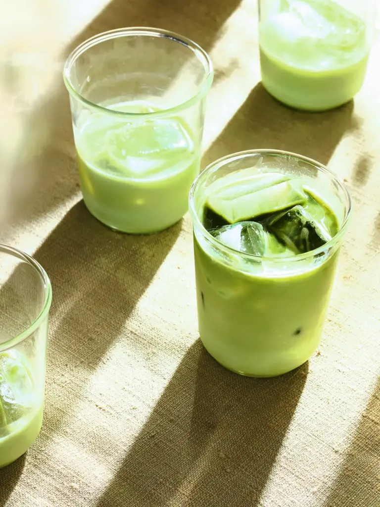 Glasses of iced green drinks casting long shadows on a textured table