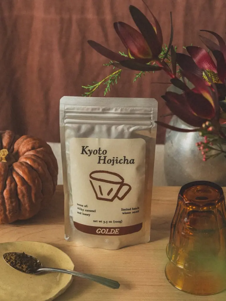 Golde Kyoto Hojicha pouch beside a pumpkin, flowers, spoon, and amber glass