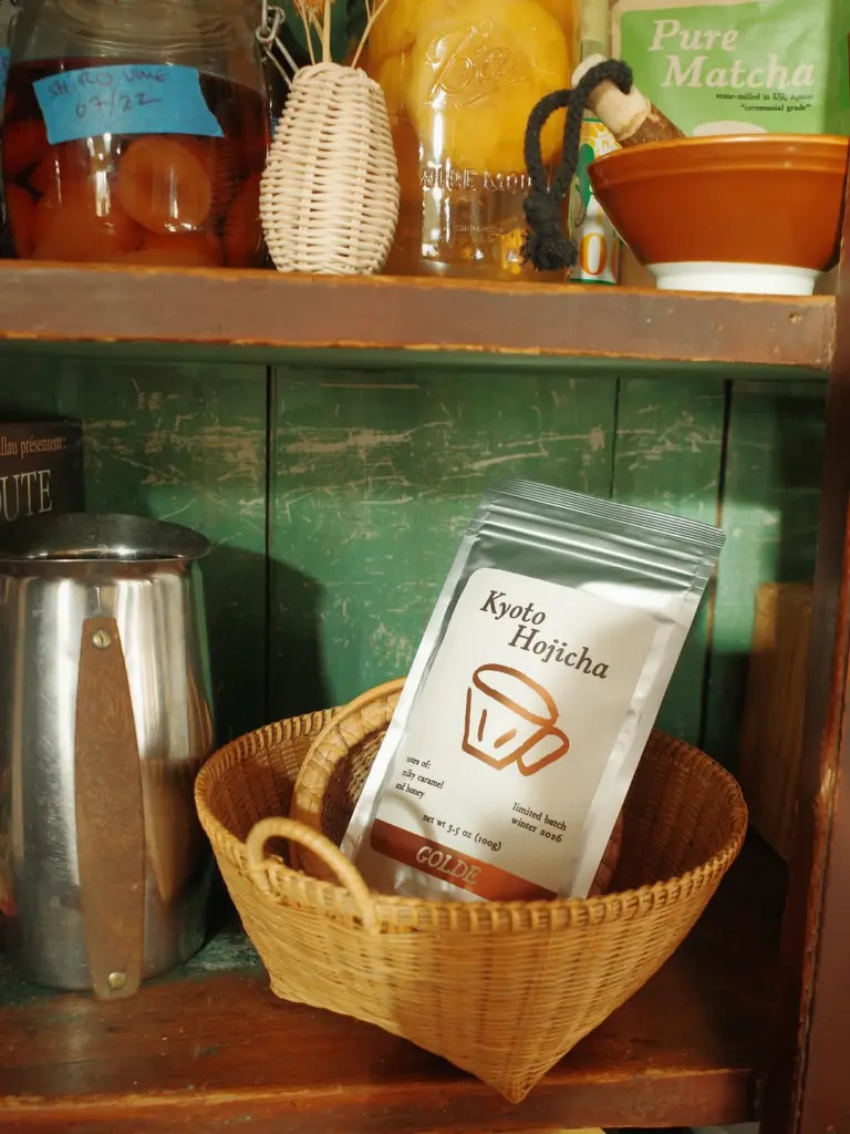 Golde Kyoto Hojicha pouch resting in a wicker basket on a green cabinet shelf