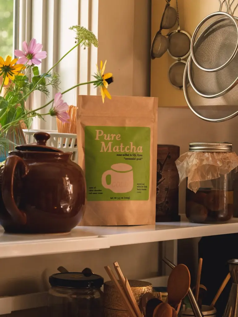 Golde Pure Matcha pouch on a kitchen shelf with flowers, teapot, jar, and strainers