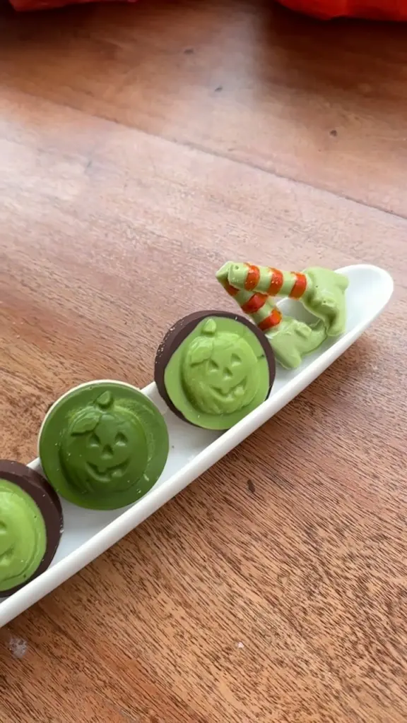 Green pumpkin-shaped confections and striped treats on a white serving dish