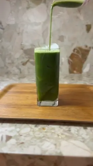 Green drink being poured into a tall glass filled with ice