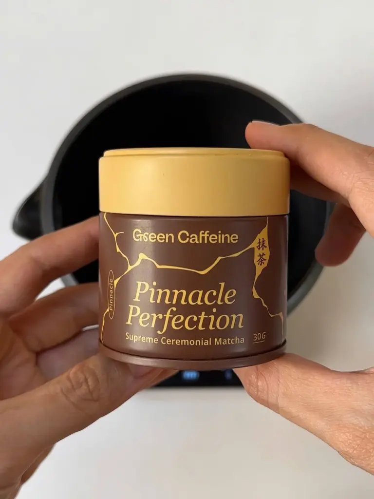 Hands holding a brown and gold Pinnacle Perfection matcha tin