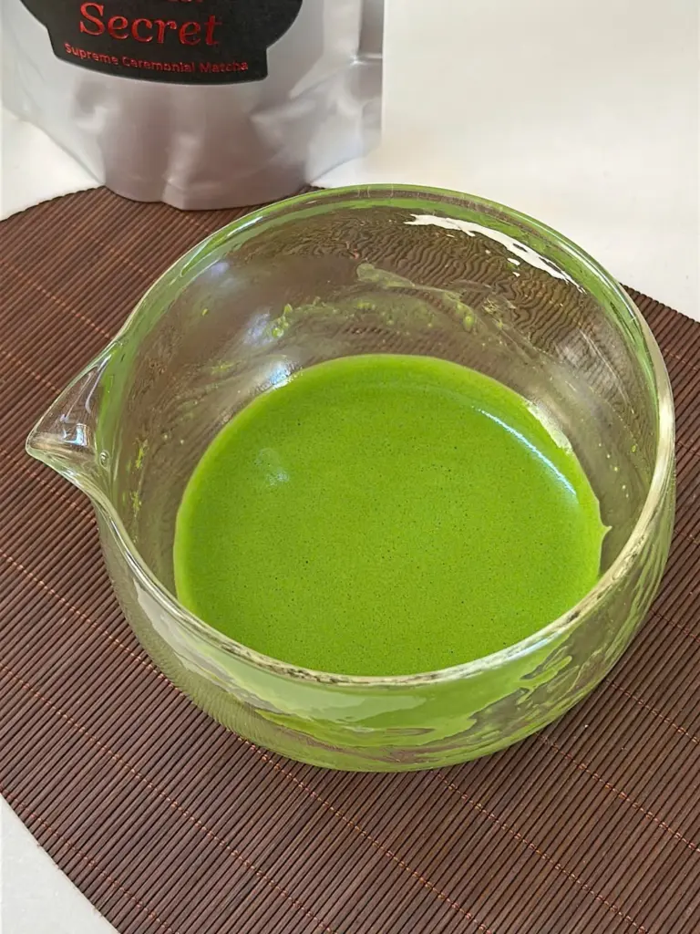 Prepared bright green matcha in a clear glass bowl