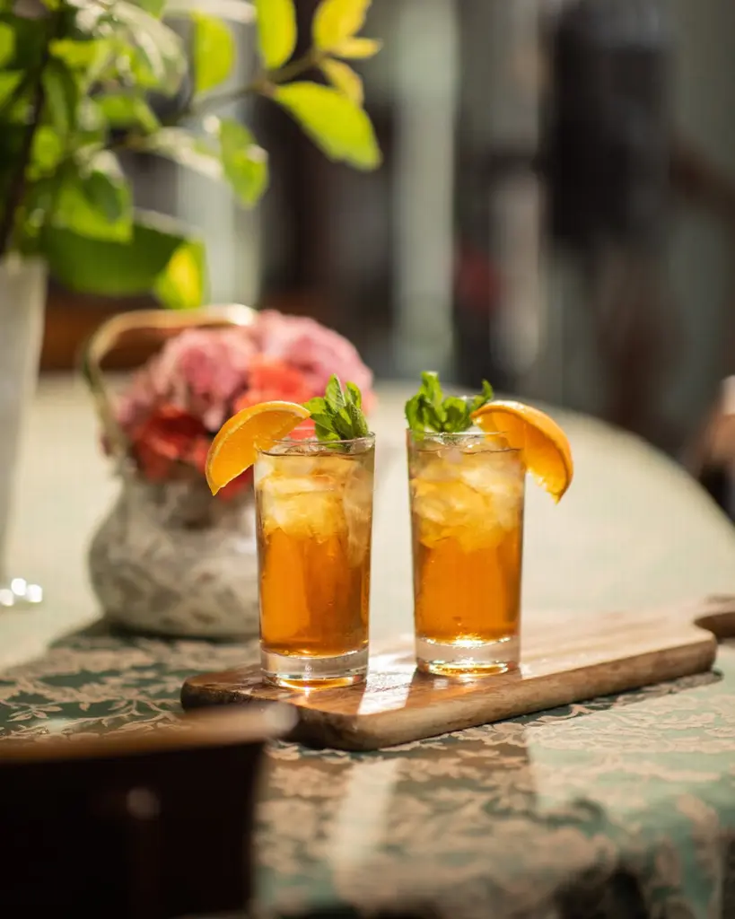 Two glasses of iced tea garnished with orange wedges and mint
