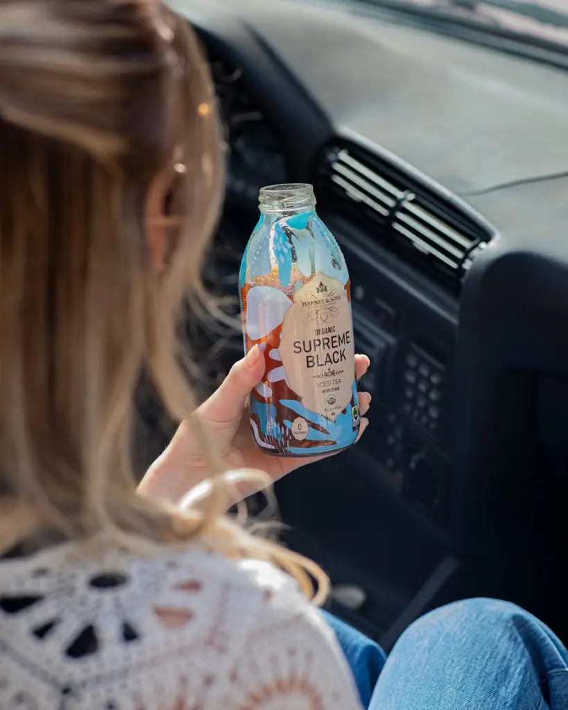Passenger holding an open Harney & Sons Supreme Black iced tea bottle in a car
