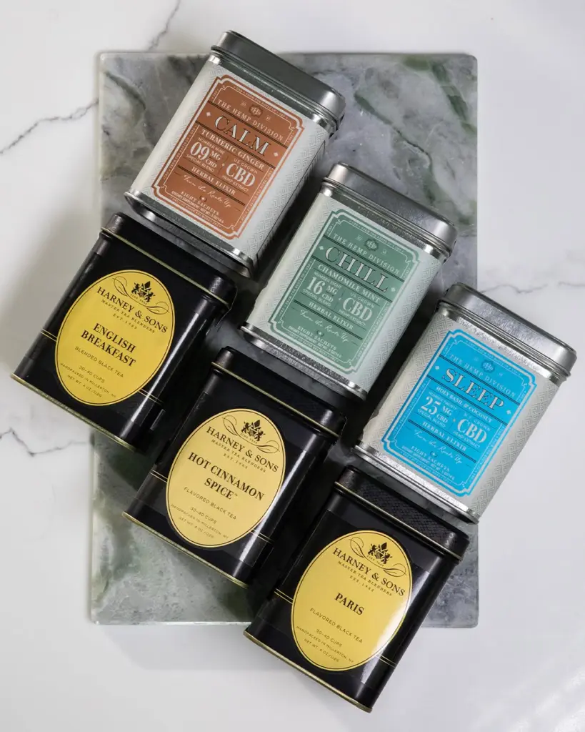 Six labeled tea and herbal elixir tins arranged on a marble board