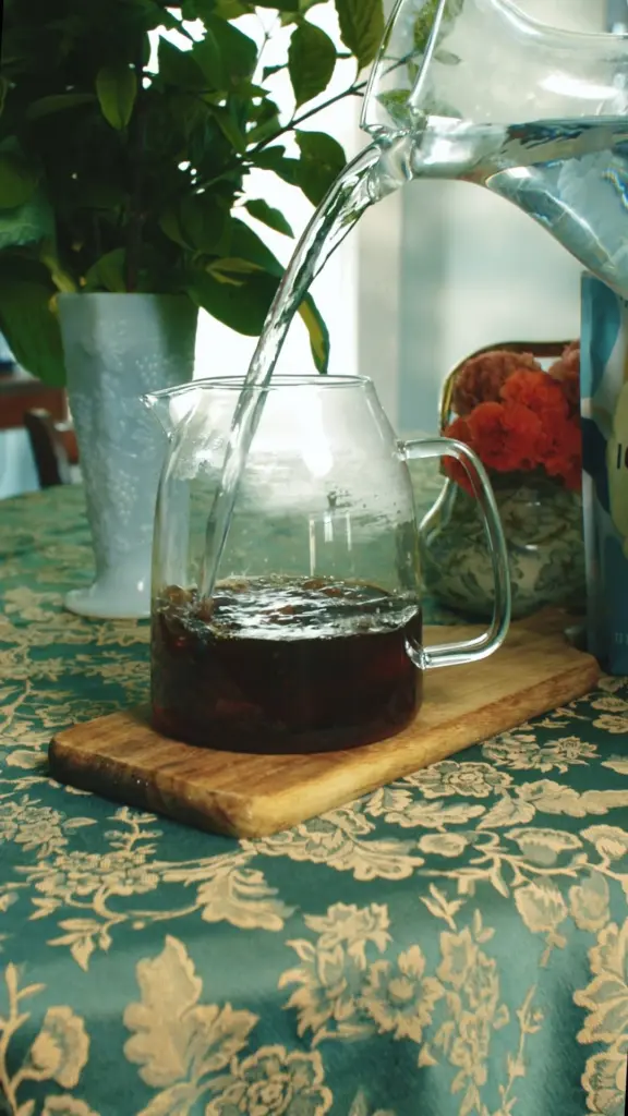 Water pouring into a glass pitcher containing dark tea