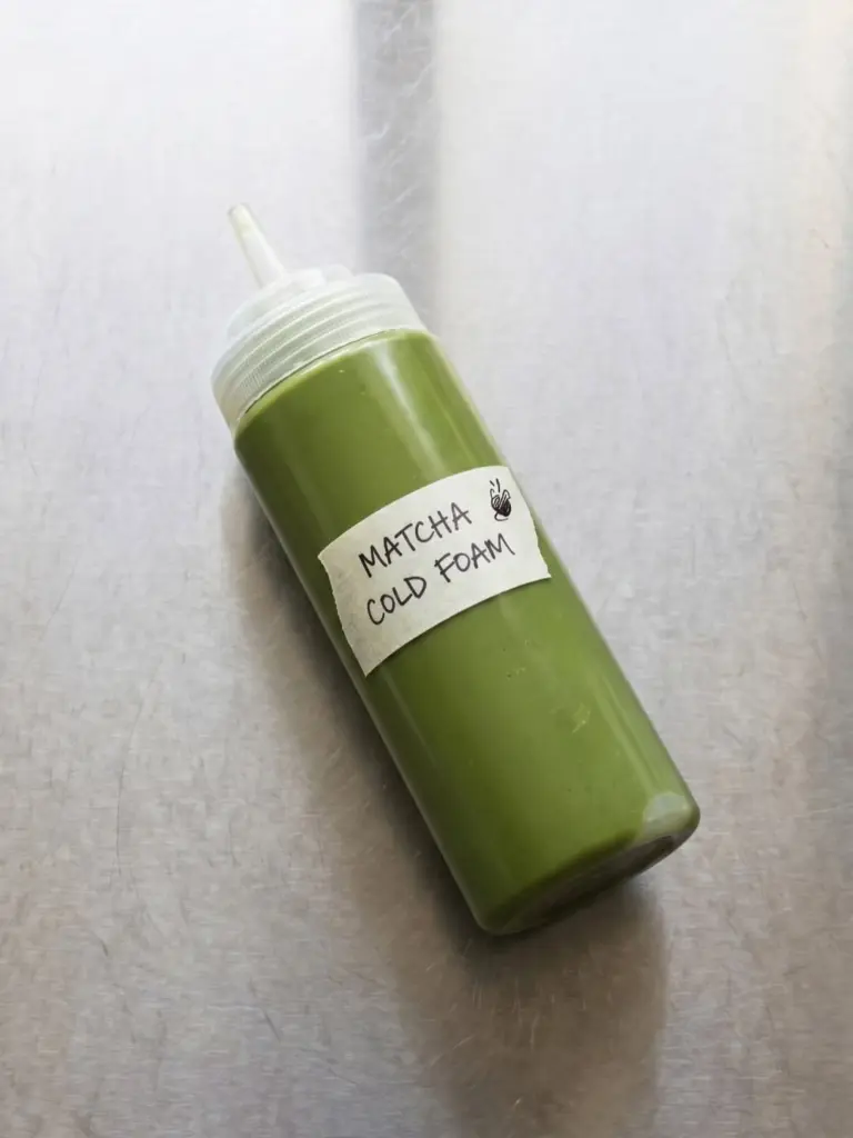 Squeeze bottle of green matcha cold foam on a metal counter