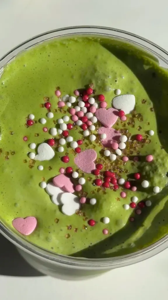 Frothy green drink topped with pink and white hearts and colorful sprinkles