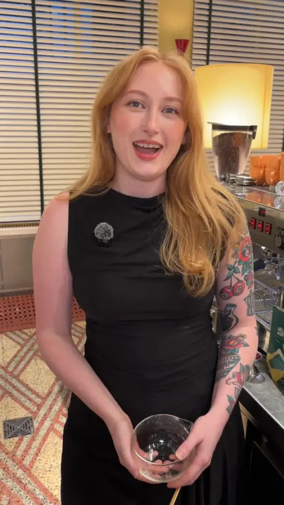 Smiling person holding a glass bowl beside café equipment