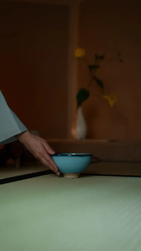 Hand placing a blue ceramic tea bowl on tatami