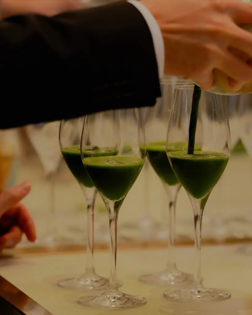 Dark green tea being poured into rows of stemmed glasses
