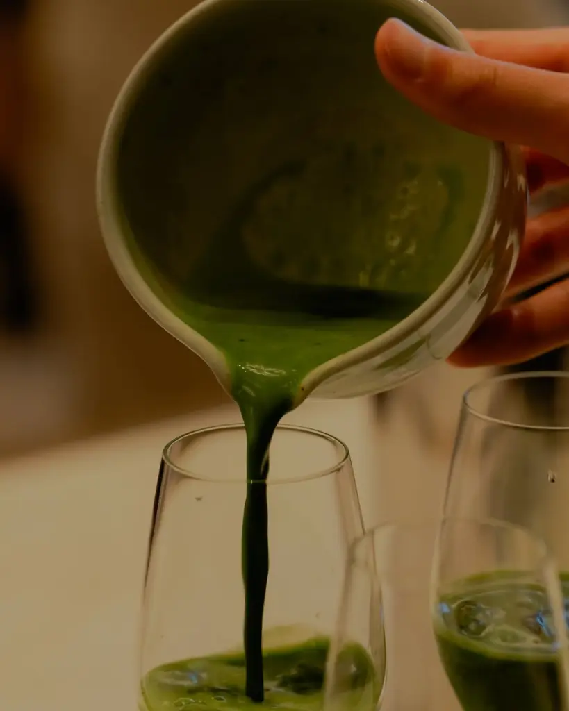 Thick green matcha pouring from a ceramic bowl into a glass