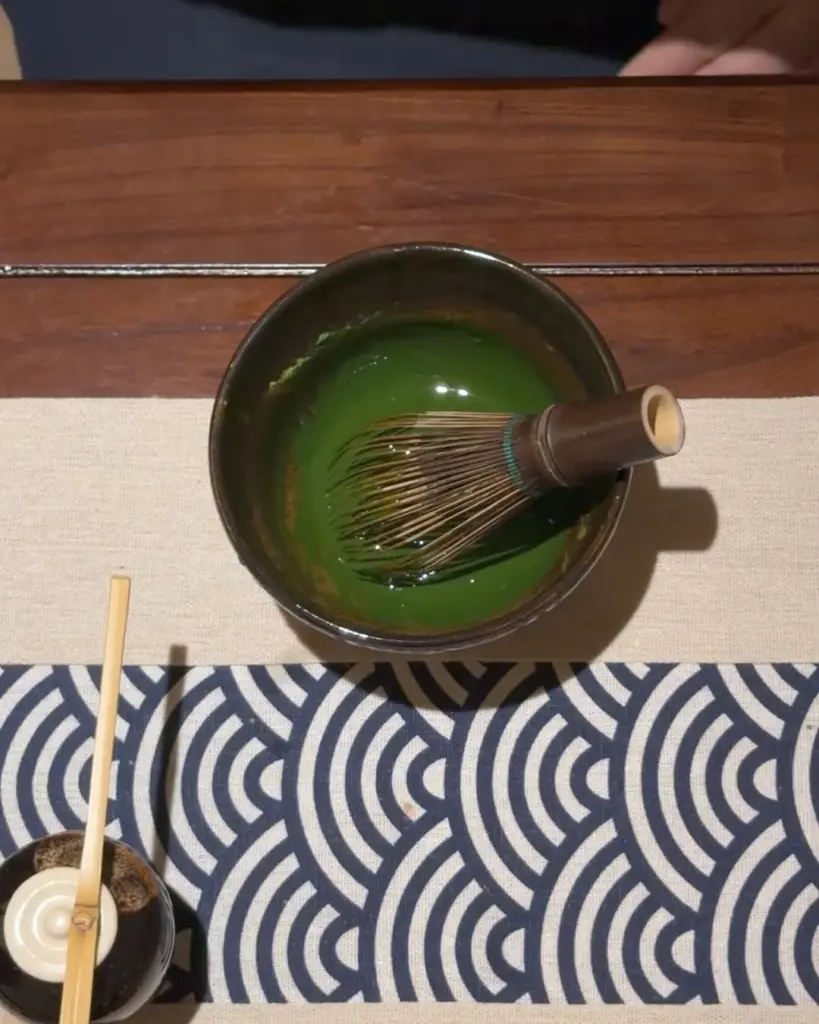 Bamboo whisk resting in a dark bowl of vivid green matcha