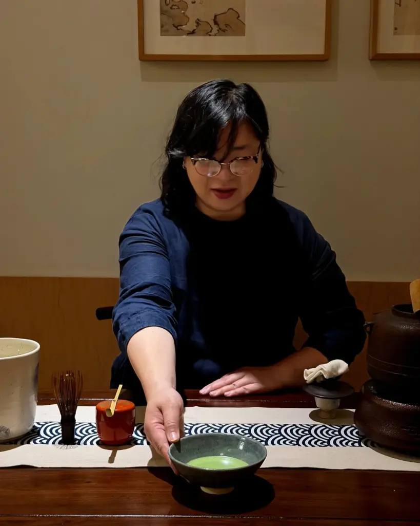 Person placing a ceramic bowl of green tea on a wooden counter